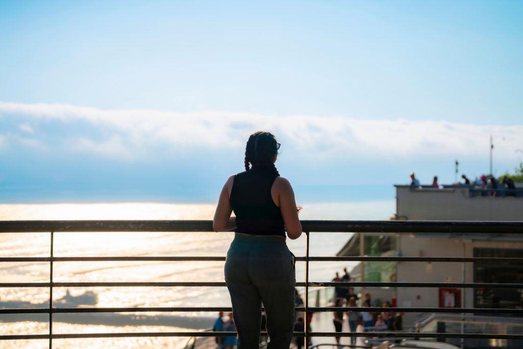 Unrecognizable young Latina woman smiling and enjoying the ocean view on a sunny day in Larcomar, Miraflores, Lima, Peru, with the coastline and mountains in the background.
