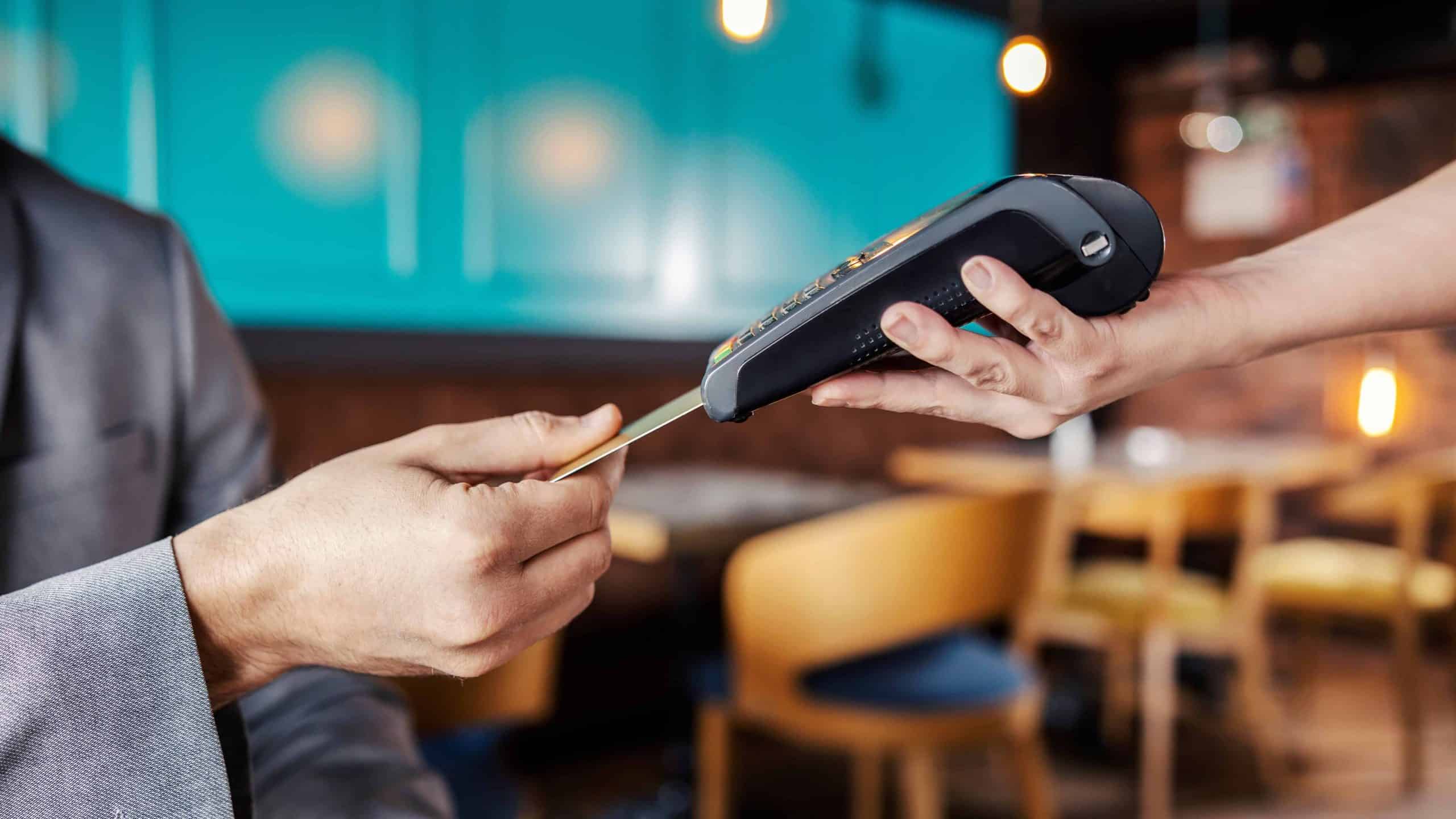 Hands holding a payment terminal. A man elegantly dressed in a business suit puts a credit or debit card in an online payment terminal held by a feminine hand. Paying bills for a meal at a restaurant