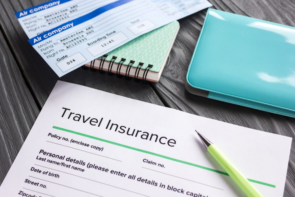 Travel insurance application form with flight tickets and passport on gray wooden desk background